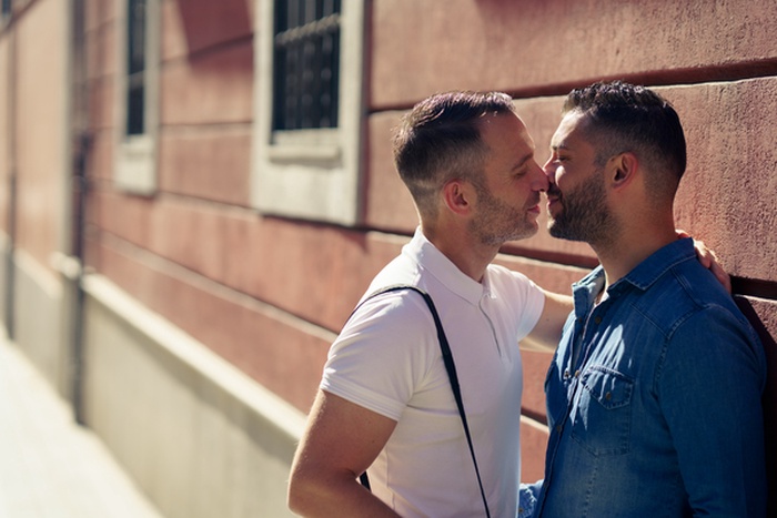 Cheerful young gay couple sitting together Two affectionate male lovers smiling cheerfully while